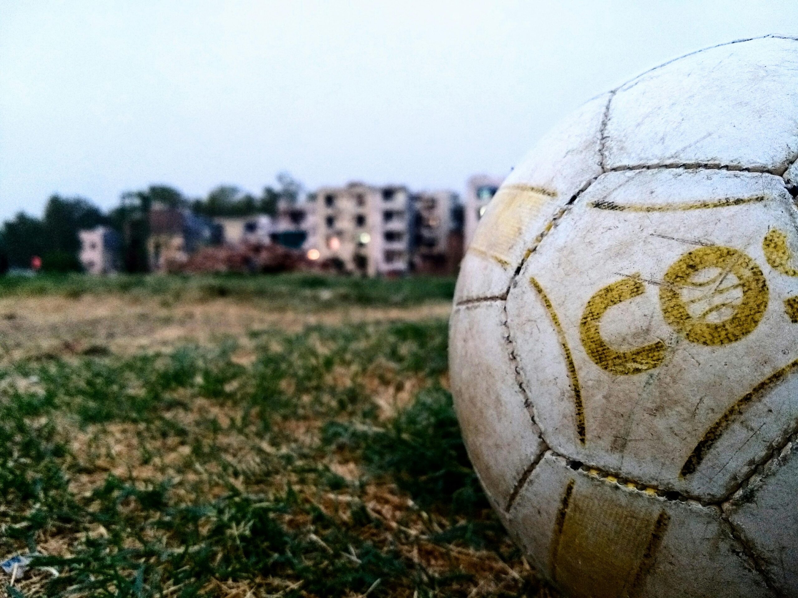 Soccer ball on a field in front of urban buildings.
